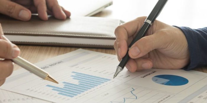 Two people with pens writing and looking at graphs