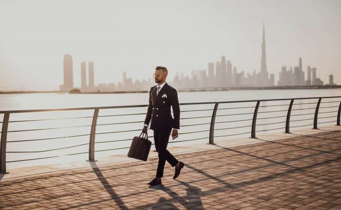 man in suit walking on the footpath with highrise buildings in the distance