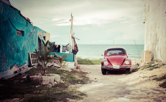 view of an old red car with the beautiful ocean behind