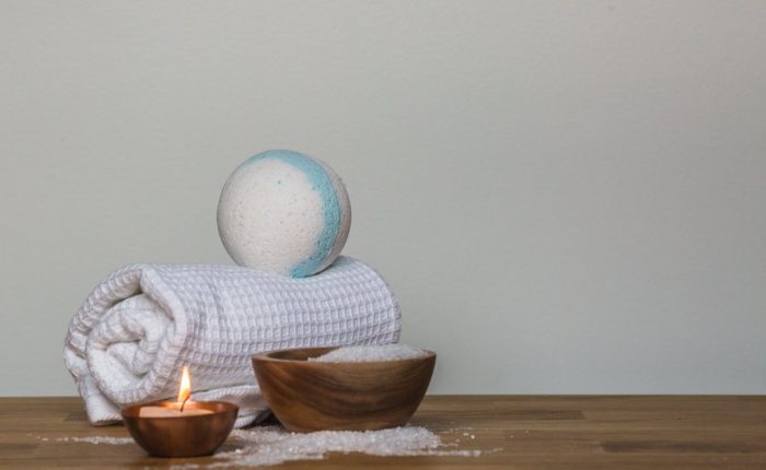 rolled up towel, a bath bomb, bath salts and a candle