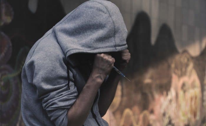 Man in grey hoodie holding a drug needle