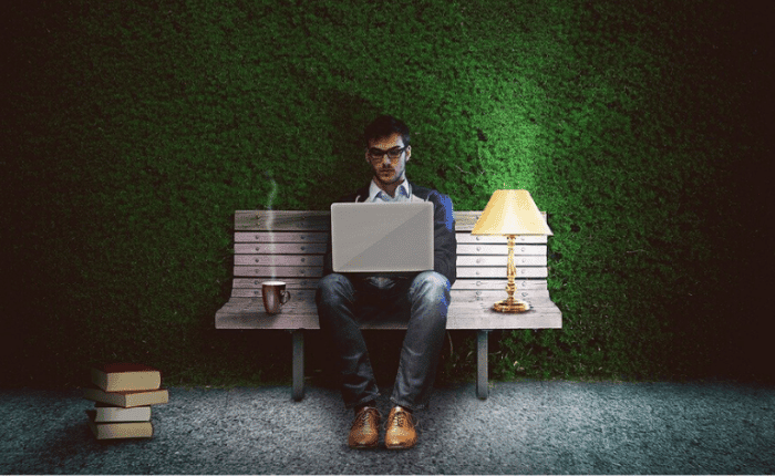 Man sitting on bench outside with a laptop and a lamp